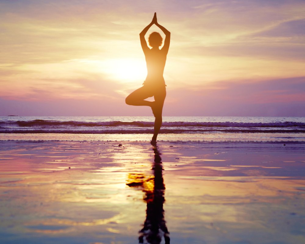 Woman in a yoga pose on the beach at sunset
